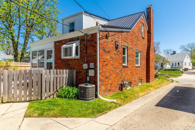 view of side of home with brick siding, central AC, fence, and a chimney