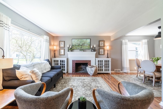 living room featuring a brick fireplace, baseboards, visible vents, and wood finished floors