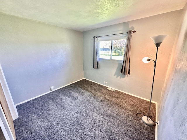 spare room with baseboards, dark carpet, and visible vents