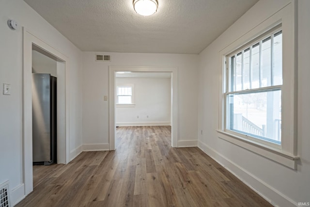 interior space featuring visible vents, baseboards, a textured ceiling, and wood finished floors