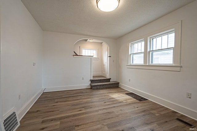 unfurnished room with visible vents, arched walkways, baseboards, and wood finished floors