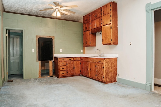 kitchen with brown cabinetry, a ceiling fan, light colored carpet, a sink, and light countertops
