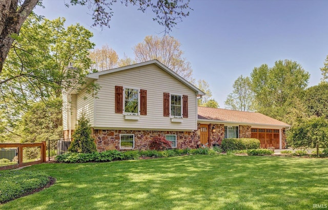 tri-level home with a garage, fence, a front yard, and stone siding