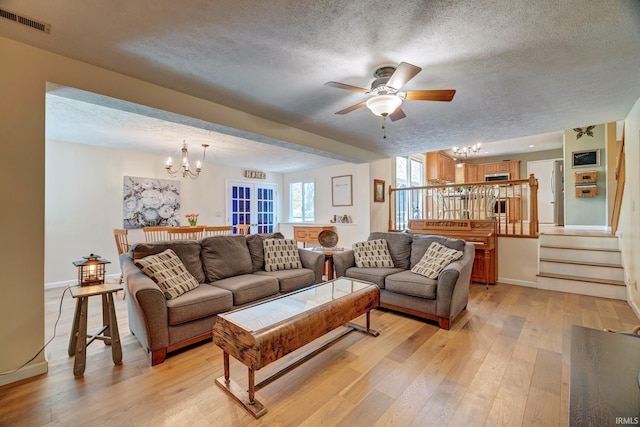 living room with light wood-style flooring, ceiling fan with notable chandelier, a textured ceiling, and visible vents