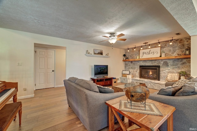 living room featuring ceiling fan, a textured ceiling, rail lighting, baseboards, and light wood finished floors