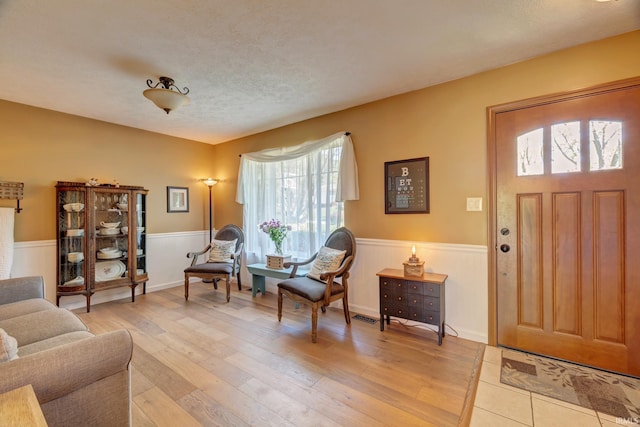 foyer entrance with visible vents, light wood-style flooring, and wainscoting