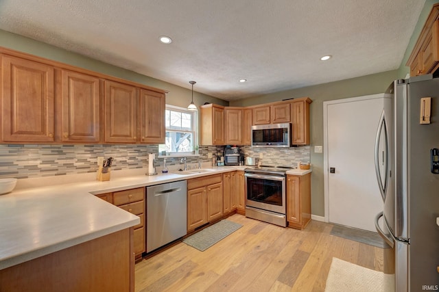 kitchen with appliances with stainless steel finishes, a sink, light wood finished floors, tasteful backsplash, and pendant lighting