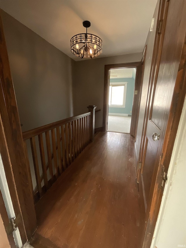 corridor with baseboards, a chandelier, and wood finished floors