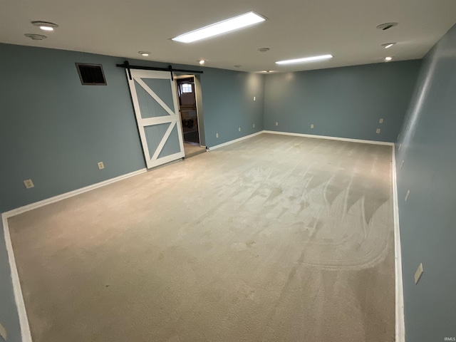 finished below grade area with visible vents, a barn door, carpet, and baseboards