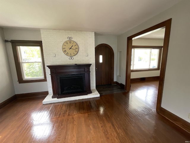 unfurnished living room with baseboards, a brick fireplace, arched walkways, and wood finished floors