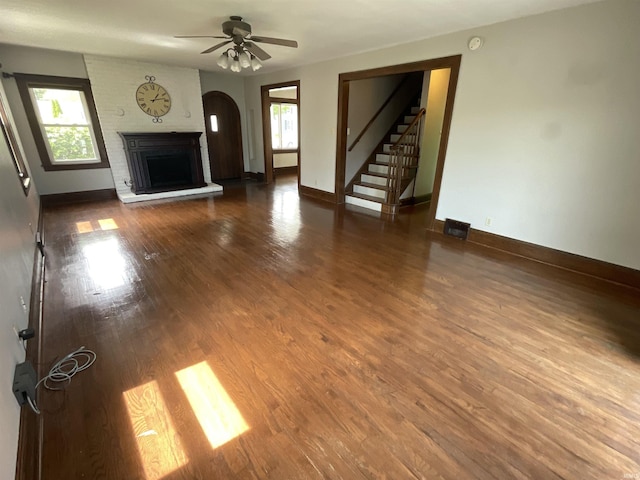 unfurnished living room featuring arched walkways, a ceiling fan, baseboards, wood finished floors, and stairway