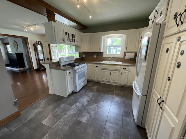 kitchen with rail lighting, a sink, baseboards, white cabinets, and white appliances
