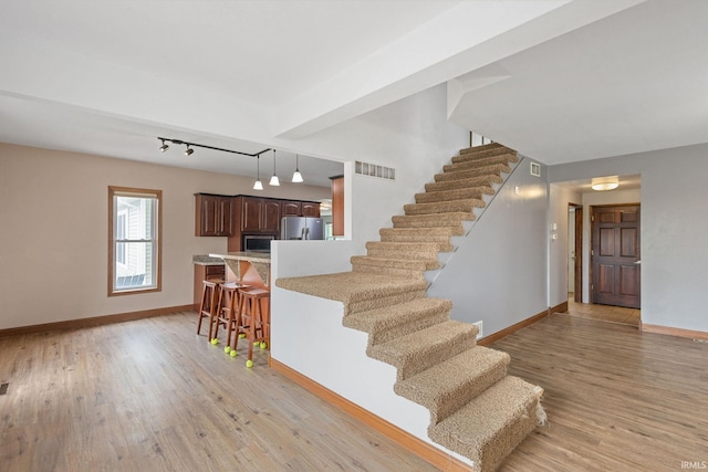 stairway featuring track lighting, baseboards, wood finished floors, and visible vents