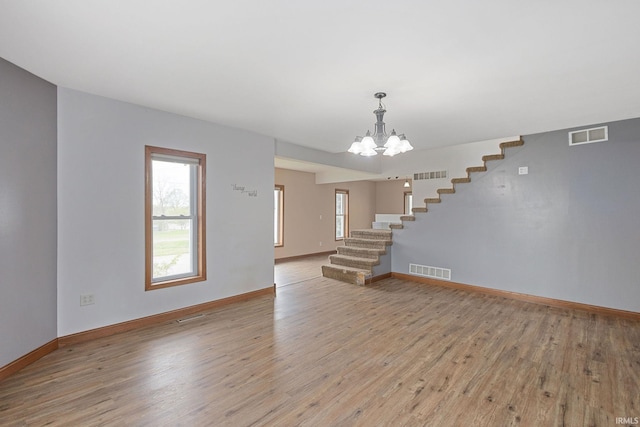 unfurnished living room featuring visible vents, stairs, light wood finished floors, and an inviting chandelier