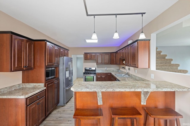 kitchen with a peninsula, light countertops, a sink, light wood-style flooring, and stainless steel appliances