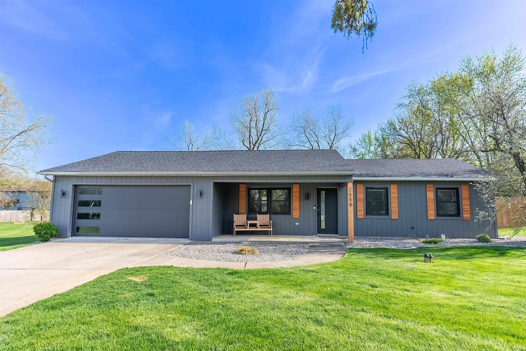 single story home featuring concrete driveway, an attached garage, covered porch, and a front yard