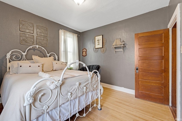bedroom with light wood-type flooring, a textured wall, and baseboards