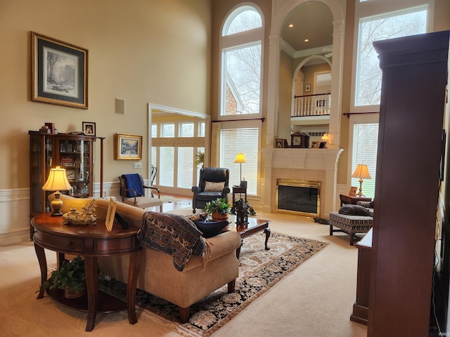 carpeted living room with a glass covered fireplace, a wainscoted wall, visible vents, and a towering ceiling
