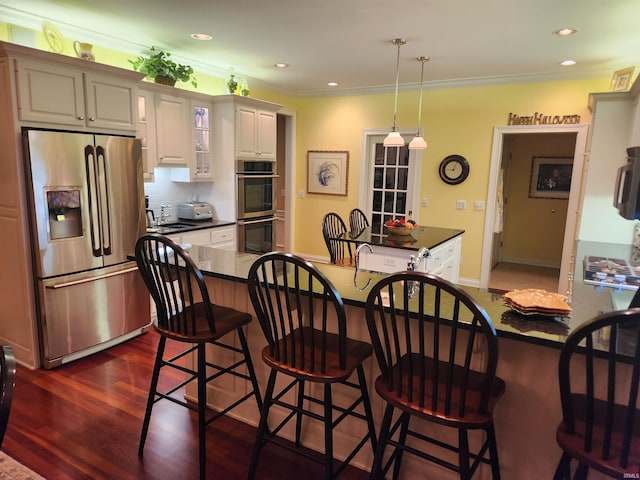kitchen featuring crown molding, dark countertops, hanging light fixtures, stainless steel appliances, and a kitchen bar