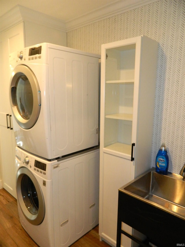 laundry area with crown molding, stacked washer and dryer, laundry area, wallpapered walls, and wood finished floors