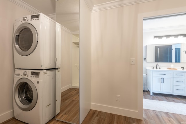 clothes washing area with stacked washer and dryer, a sink, baseboards, light wood-style floors, and ornamental molding