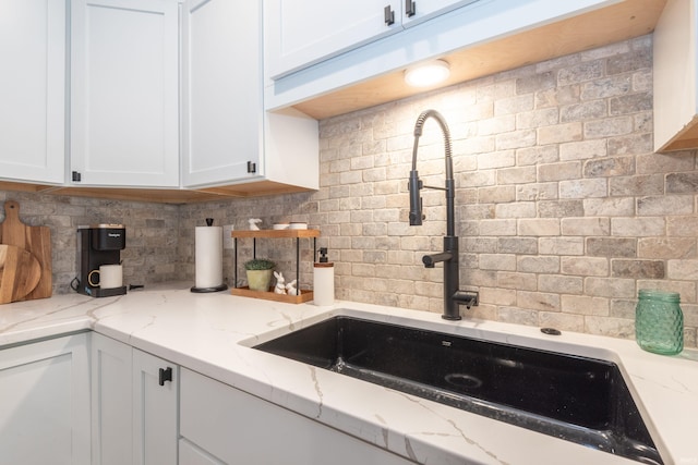 kitchen with a sink, decorative backsplash, white cabinets, and light stone countertops