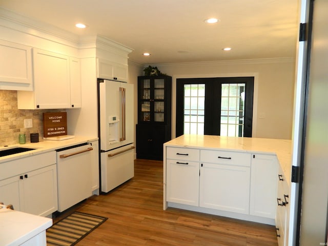 kitchen with tasteful backsplash, a peninsula, ornamental molding, white appliances, and white cabinetry