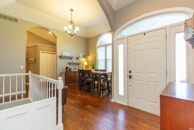entrance foyer with arched walkways, a chandelier, visible vents, and dark wood-type flooring