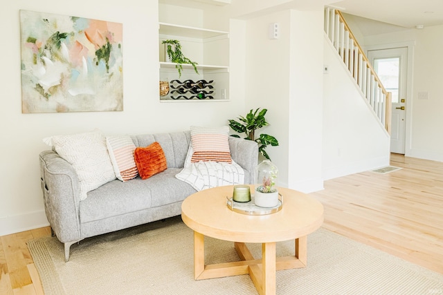 living area featuring stairs, baseboards, visible vents, and wood finished floors