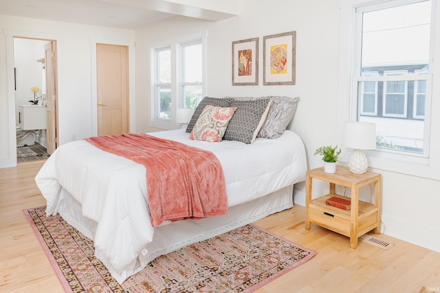bedroom featuring visible vents, light wood-style flooring, and ensuite bath