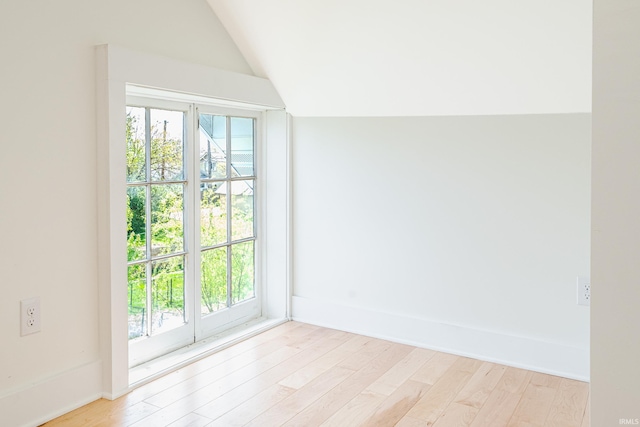 empty room featuring baseboards, light wood-style flooring, and vaulted ceiling