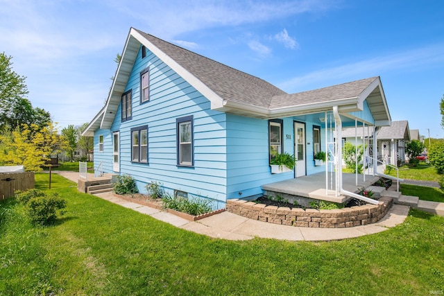 view of side of property with a shingled roof, a yard, and covered porch