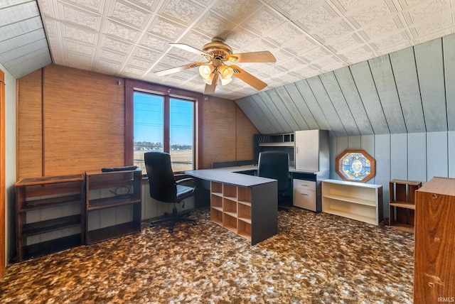 carpeted office with wooden walls, a ceiling fan, and vaulted ceiling