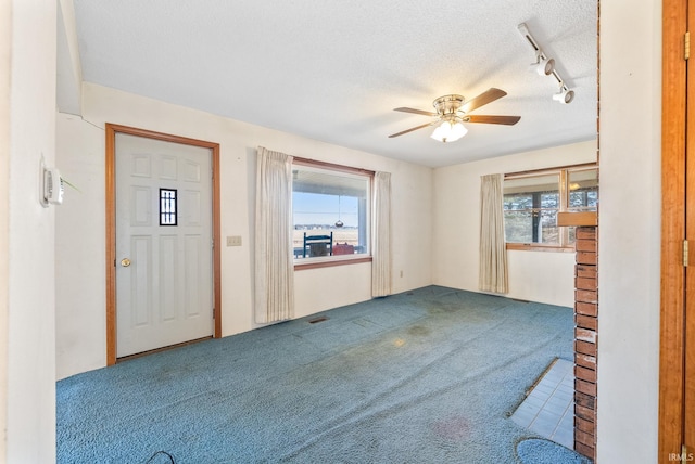 interior space with carpet floors, a ceiling fan, rail lighting, and a textured ceiling