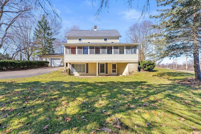 rear view of house featuring a sunroom, a lawn, driveway, and a chimney