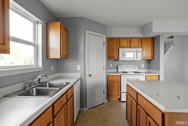 kitchen with brown cabinetry, light countertops, a sink, and white appliances