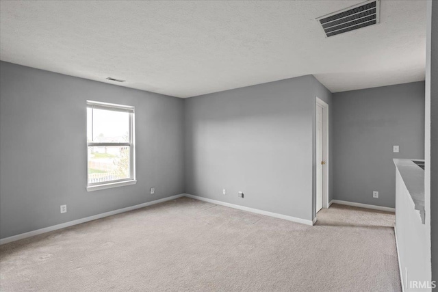 unfurnished room featuring a textured ceiling, baseboards, visible vents, and light carpet