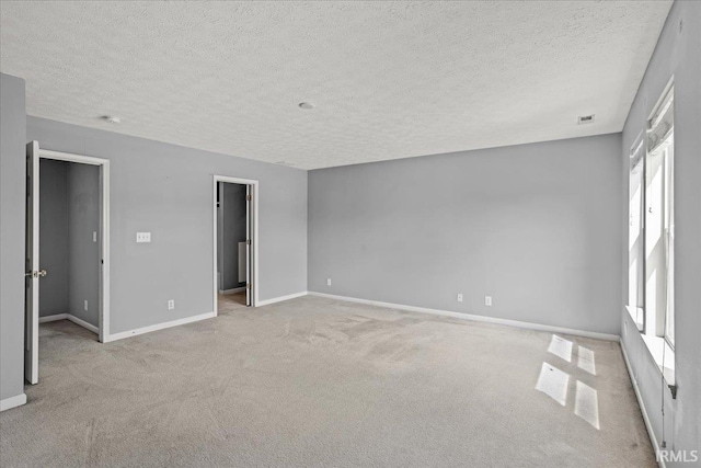unfurnished bedroom with baseboards, a textured ceiling, light carpet, and a walk in closet