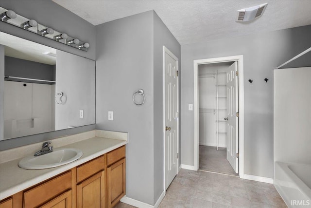 full bathroom with vanity, a bathing tub, a textured ceiling, baseboards, and visible vents