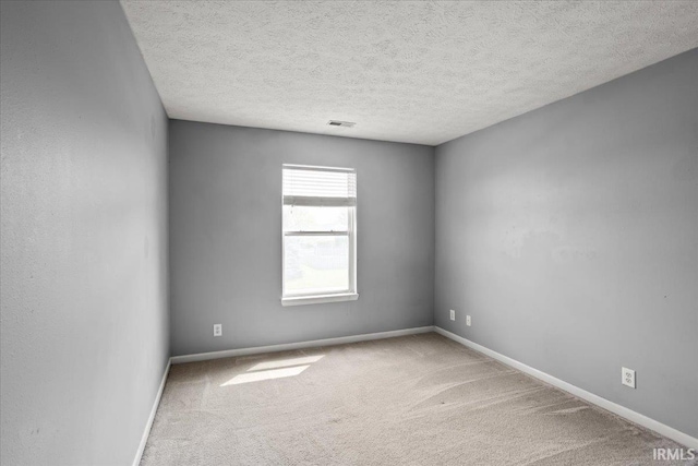 spare room with carpet floors, a textured ceiling, baseboards, and visible vents