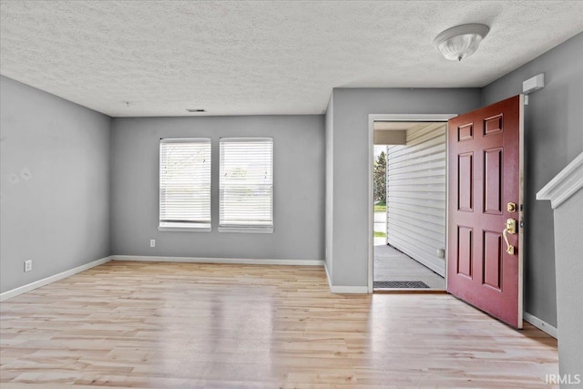 foyer entrance with baseboards, a textured ceiling, wood finished floors, and visible vents