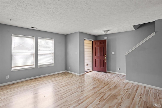 interior space featuring baseboards, a textured ceiling, wood finished floors, and visible vents