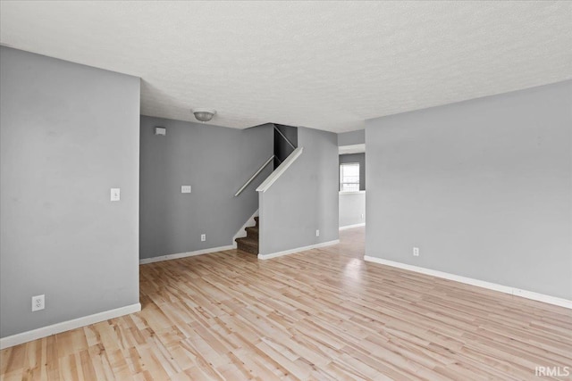 unfurnished living room with baseboards, a textured ceiling, light wood finished floors, and stairs