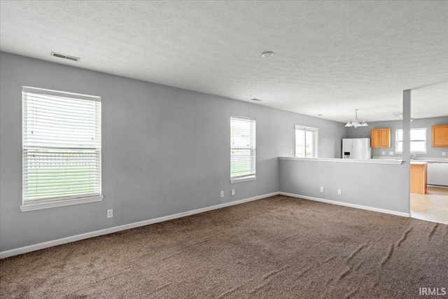 unfurnished living room with a textured ceiling, visible vents, and an inviting chandelier