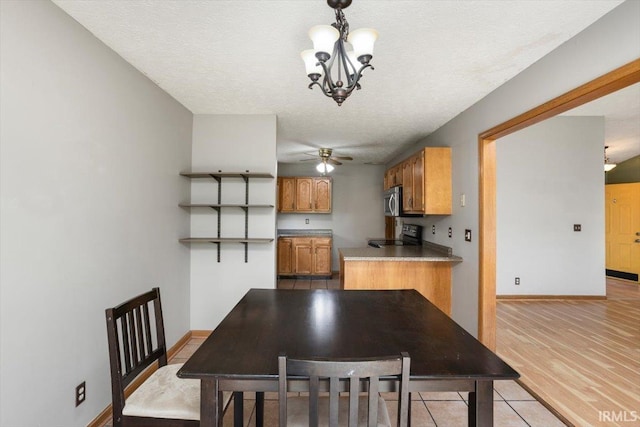 dining area featuring baseboards, ceiling fan with notable chandelier, light wood-type flooring, and a textured ceiling