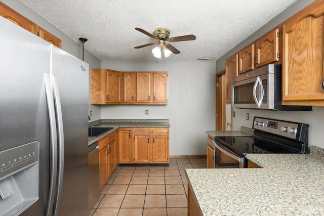 kitchen with ceiling fan, brown cabinets, light tile patterned flooring, and stainless steel appliances