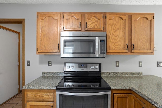 kitchen with tile patterned floors, brown cabinets, and stainless steel appliances