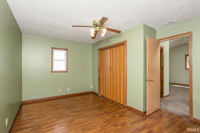 unfurnished bedroom featuring a textured ceiling, baseboards, wood finished floors, visible vents, and a closet
