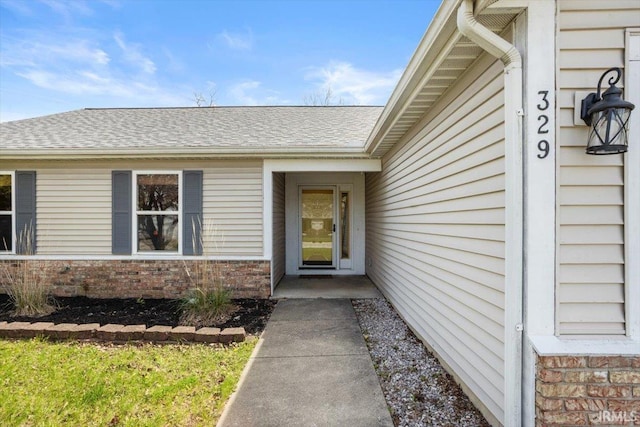 property entrance featuring brick siding and roof with shingles