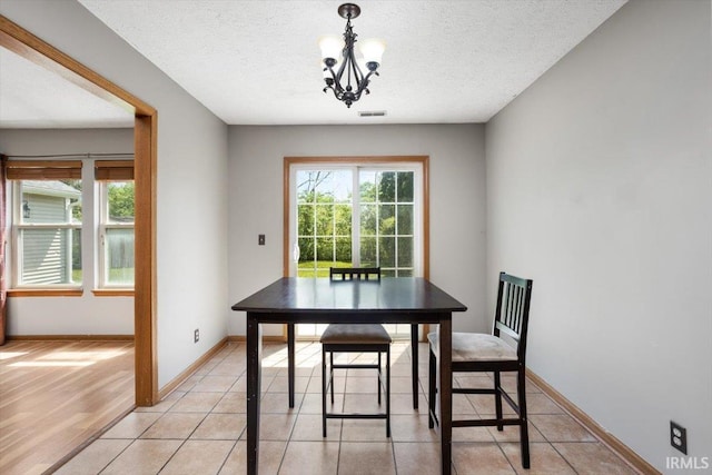 dining room featuring baseboards, a textured ceiling, a notable chandelier, and a healthy amount of sunlight